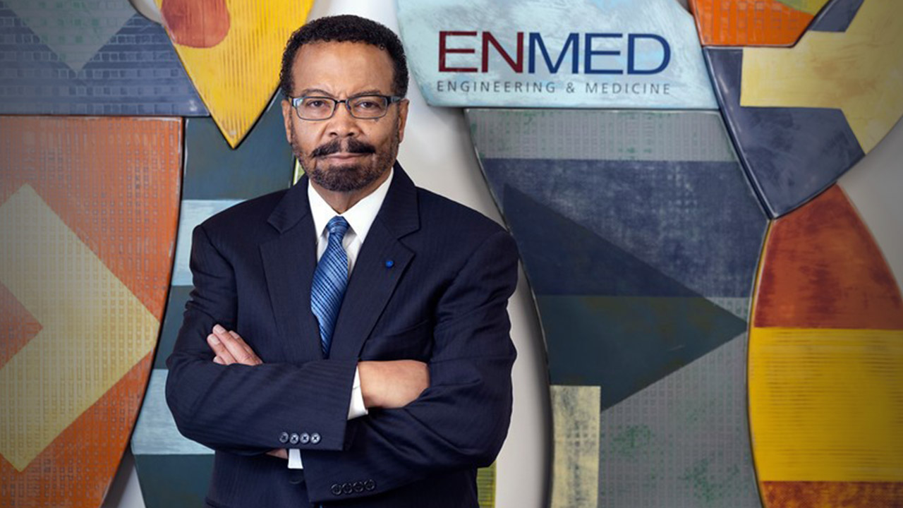 Roderic Pettigrew standing on front of a painted wall with the EnMed logo