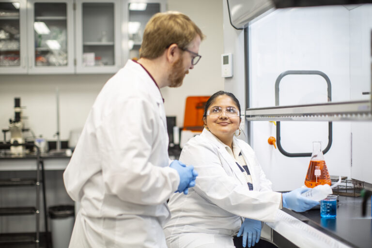 EnMed students wearing lab coats working in research facility