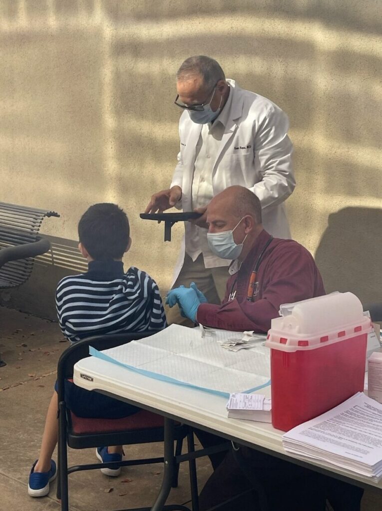 Dr. Jeremy Gibson giving child an injection with doctor standing in background